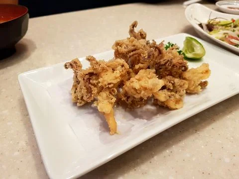 Deep fried squid with sliced lime or lemon in white dish on table Stock Photos