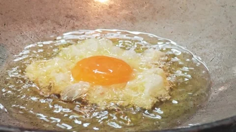 Deep frying a crispy egg with runny yolk in hot oil inside a wok. Видео 343697968