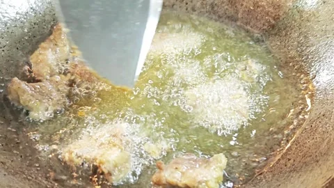 Deep frying seasoned meat inside a hot pan with bubbling oil. Видео 343697796