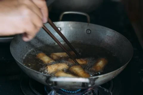 Deep frying spring rolls in a pot on the stove using chopsticks. Stock Photos