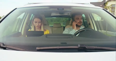Deep in gadgets. Beautiful young couple sitting on the front passenger seats and Stock Footage 157359613