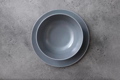 Deep grey plate on a flat grey plate on a grey concrete background, empty cer Stock Photos