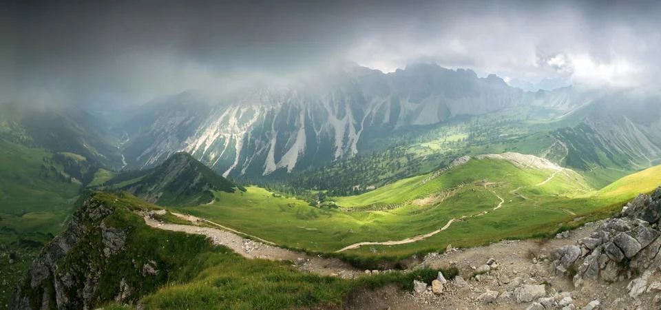 Deep hanging clouds above mountains. Mystic light breaks through fog. Stock Photos