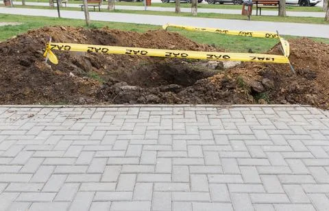 Deep hole surrounded by dirt and yellow caution tape on grassy area near pa.. Stock Photos
