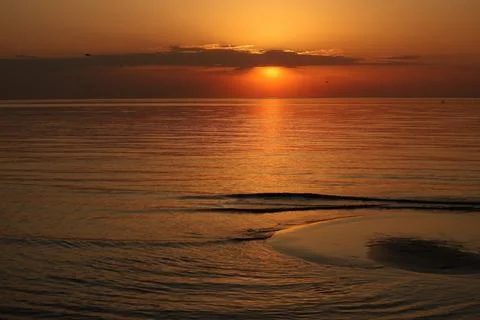 Deep orange sunset sky with a bright sun and its golden reflection illuminating Stock Photos