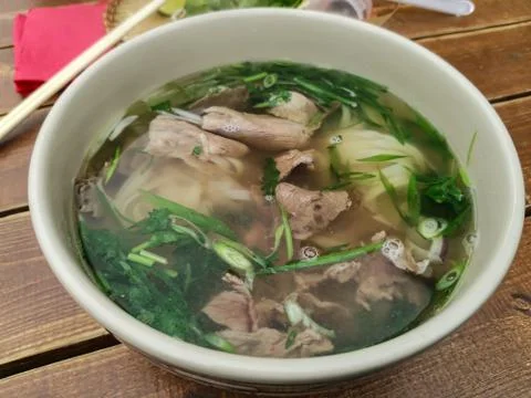 Deep plate with beef broth and herbs on a wooden table. Stock Photos