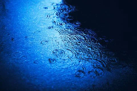 A deep puddle on the asphalt in the city, on the surface of which raindrops f Stock Photos