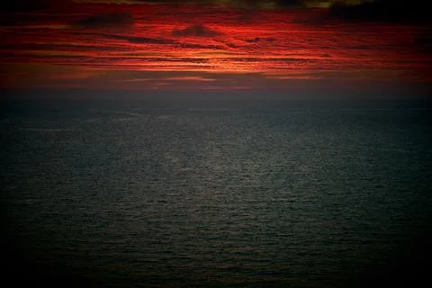 A deep red sunrise sky over a moody seascape 写真素材