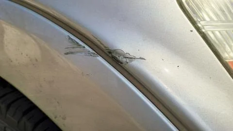 Deep scratch and peeling paint on a silver car body panel. Фото