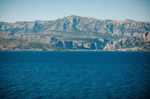 Deep sea stretching out in front of high rocky mountains Stock Photos