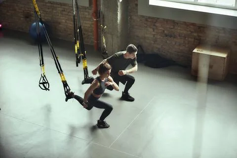 Deep squat. Young active couple in sportswear training legs with Trx fitness Stock Photos