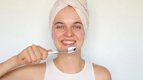 Deep teeth cleaning. Young lady wearing towel over head brushing her teeth .. 库存影片 251897624
