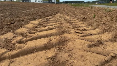 Deep tire tracks in sandy dirt field leading to distant buildings and road Vidéo 338201347