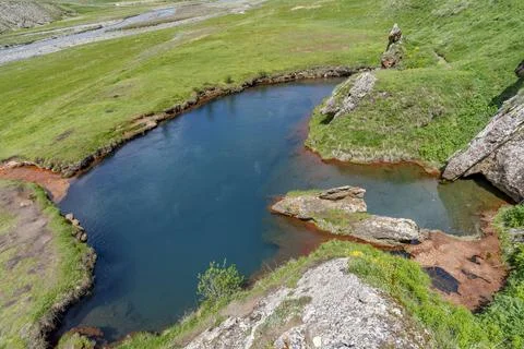 Deep turquoise spring pool beside rocks on open mountain meadow Stock Photos