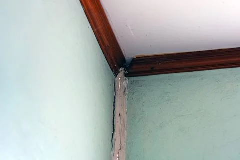Deep vertical crack in corner of residential concrete wall near wooden ceil.. Stock Photos