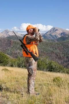 Deer hunter in mountains viewing through binoculars Stock Photos