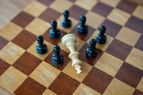 Defeated white chess king surrounded by black pawns on wooden chess board Stock Photos