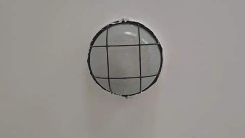 Defective round ceiling lamp with a protective metal grid flickering. The light Stock Footage 345971406