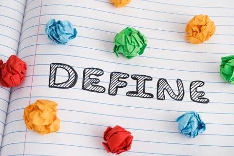 Define word on notebook sheet with some colorful crumpled paper balls on it Stock Photos