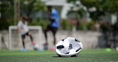 Deflated soccer ball on field with boy doing ball mastery drills in background Stock Footage 345644837