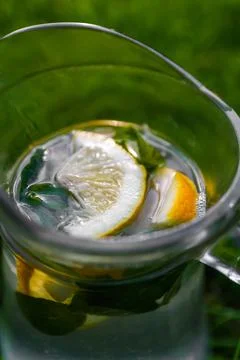 Defocus close-up lemon and mint in glass jug of lemonade on natural green nat Stock Photos