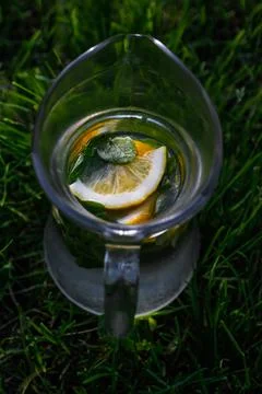 Defocus close-up slice lemon and leaves of mint in glass jug of lemonade natu Stock Photos