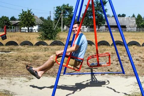 Defocus smiling young man swinging on swing on playground. Countryside area.  Фото