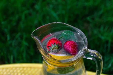 Defocus two strawberry, slice lemon and leaves of mint in glass jug of lemona Foto stock