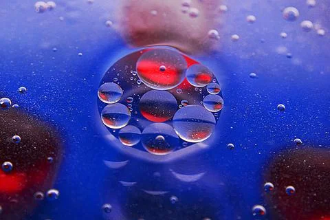 Defocused abstract background with blue and red oil bubbles in water. Macro p Stock Photos