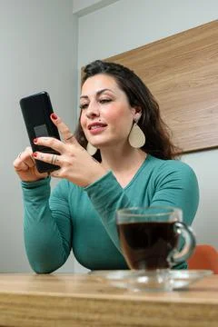 In defocused foreground, cup of coffee. In the background Brazilian woman smi Stock Photos