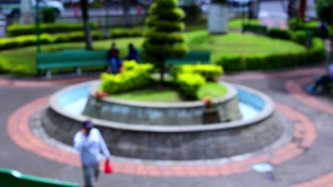 Defocused view, unrecognisable people walking around a fountain in a park Stock Footage 155296046