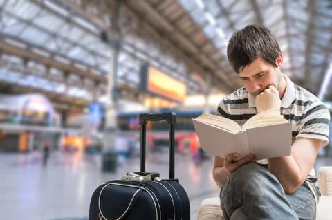 Delayed train concept. Man is sitting in train station and reading book. Foto stock