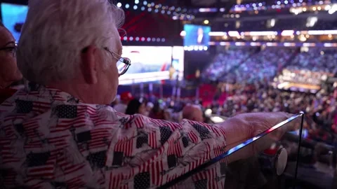 A delegate in an American flag shirt gestures toward the stage from the stands Stock Footage 345271340