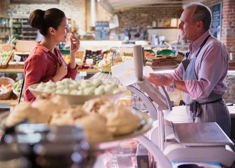 Deli worker offering cheese sample to woman in market Stock Photos
