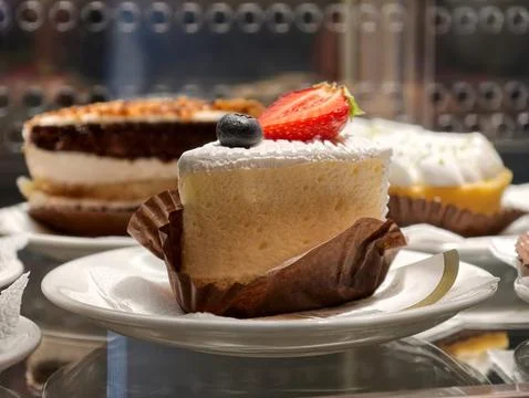 A delicate cake slice on a small plate stands in a confectionery display ca.. Stock Photos