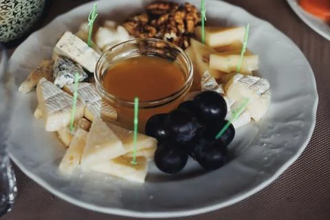 Delicate cheeses, grapes, and nuts arranged on a rustic plate Stockfoto's