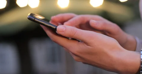 Delicate female hands scrolling something on cell phone. Evening lights on the Stock Footage 104618769