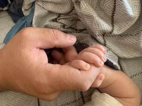 The delicate moment of a baby's tiny hand gently gripping an adult's finger Foto stock