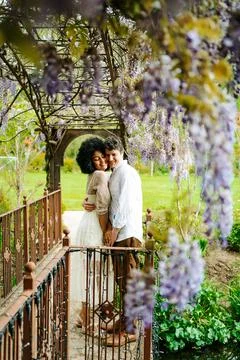 Delicate multiethnic couple hugging under natural arch of flowers Stock Photos