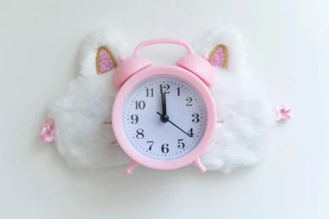 Delicate pink alarm clock on the background of a light-permeable sleep band o Stock Photos