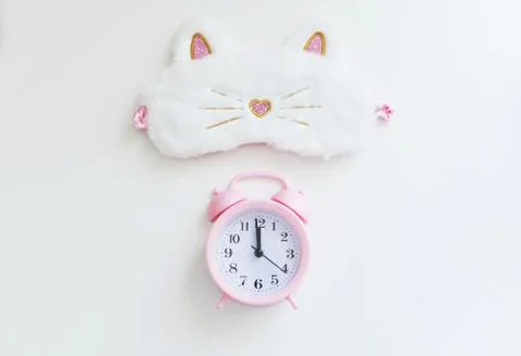 Delicate pink alarm clock on the background of a light-permeable sleep band o Stock Photos
