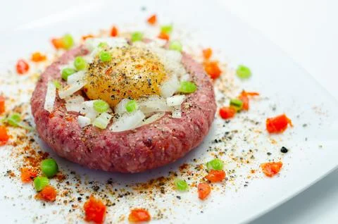 Delicate raw beef patty garnished with egg yolk and chopped onion Stock Photos
