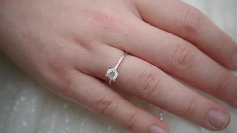 A delicate silver engagement ring with a sparkling diamond worn on a finger.. Stockbeeldmateriaal 316274824