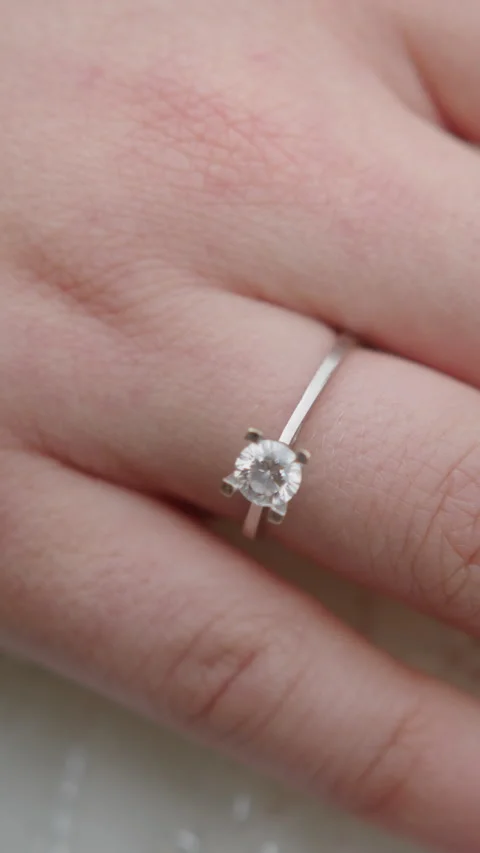 A delicate silver engagement ring with a sparkling diamond worn on a finger.. Stockbeeldmateriaal 316279726