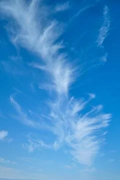 Delicate wispy cirrus clouds stretch across a vivid blue sky, creating an air Stock Photos