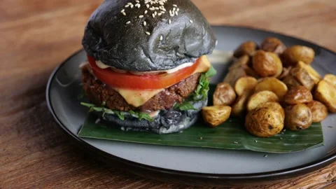 Delicious appetizing black burger with beef patty, tomato, melted cheese and Stock Footage 235698092