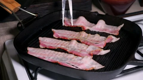 Delicious bacon slices being cooked, then being flipped by cooking tongs. 스톡 동영상 334642457