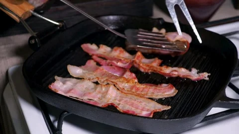 Delicious bacon slices being cooked, then being flipped by cooking tongs. 스톡 동영상 334642480