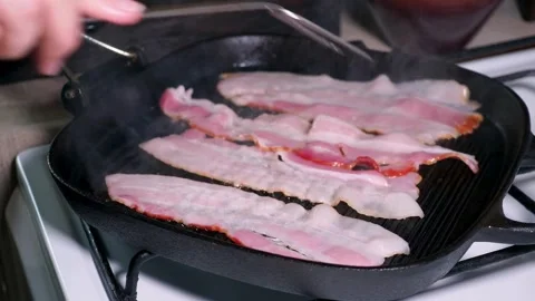 Delicious bacon slices being cooked, then being flipped by cooking tongs. 스톡 동영상 334642487