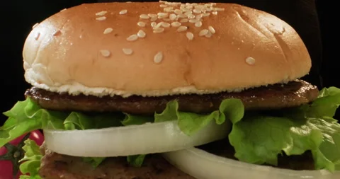 Delicious big hamburger preparation. Half of bun with sesame seed falling on Stock Footage 293850610
